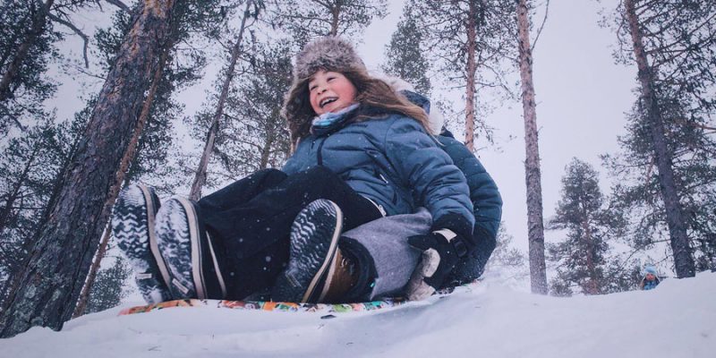 Kind fährt im Schnee Schlitten in Lappland
