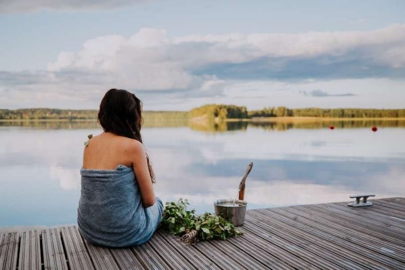 Frau sitzt auf einem Steg vor einem See und enstpannt nach Welness