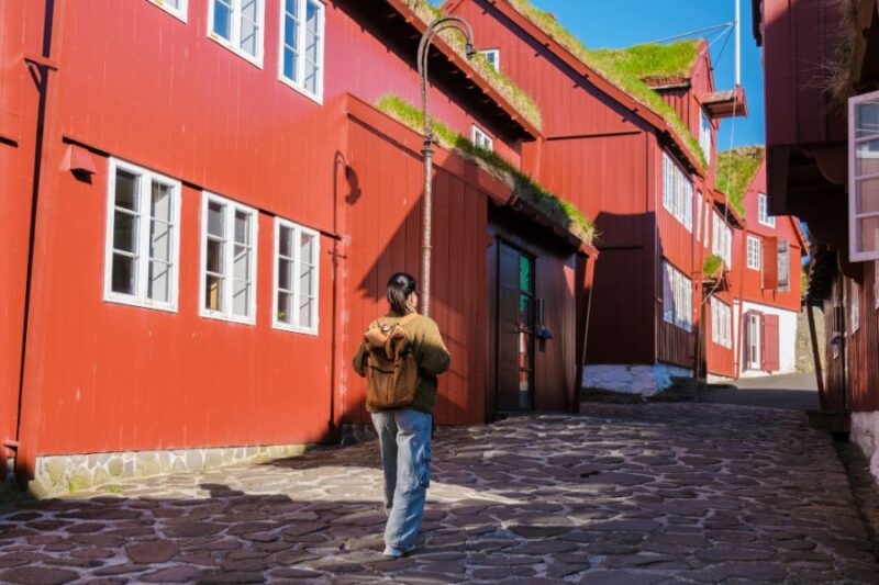 Eine-Frau-laeuft-durch-eine-charmante-Strasse-in-Torshavn-mit-bunten-Gebaeuden-auf-den-Faeroeer-Inseln-Reisen-nach-Skandinavien-mit-Nordic