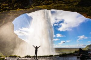 Person-steht-hinter-Seljalandsfoss-Wasserfall-in-Island-im-Sommer-Reisen-mit-Nordic-der-Skandinavien-Spezialist