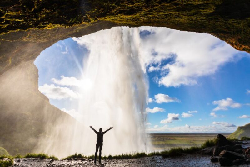 Person-steht-hinter-Seljalandsfoss-Wasserfall-in-Island-im-Sommer-Reisen-mit-Nordic-der-Skandinavien-Spezialist