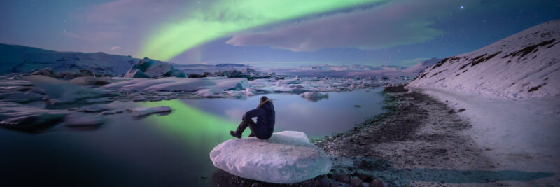Person-sitzt-in-Gletscher-Lagune-in-Island-mit-Nordlichtern-am-Himmel-Reisen-mit-Nordic-der-Skandinavien-Spezialist